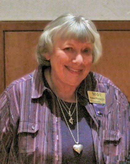 A woman in a purple shirt is smiling at the camera.