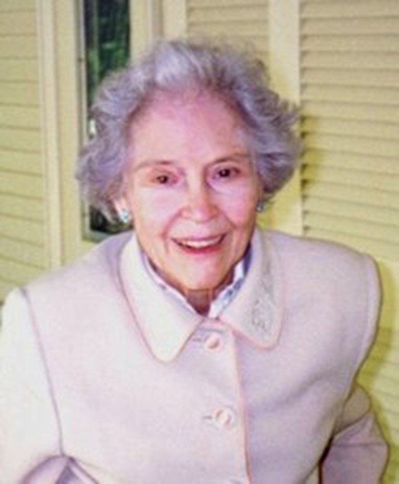 An older woman in a white coat is smiling.