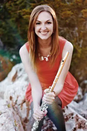 A young woman smiling while holding a flute.