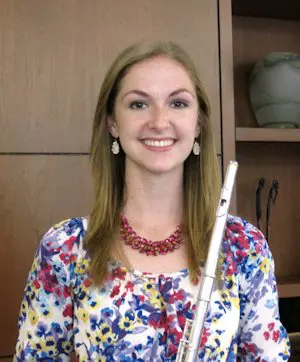 A young woman smiling while holding a flute.