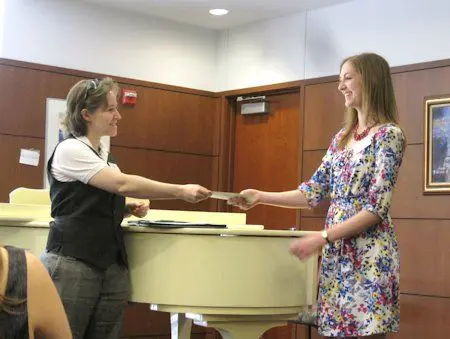Two women shaking hands in front of a piano.