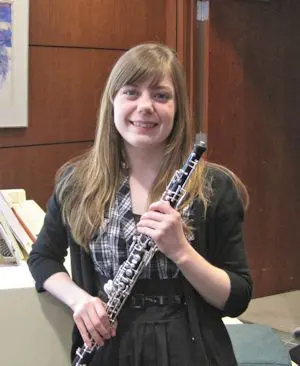 A young woman smiling while holding a clarinet.