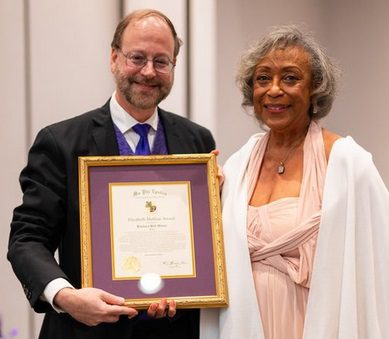A man and woman standing next to each other holding a framed certificate.