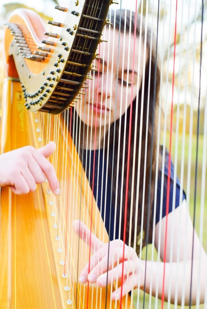 A young woman playing a harp in a park.
