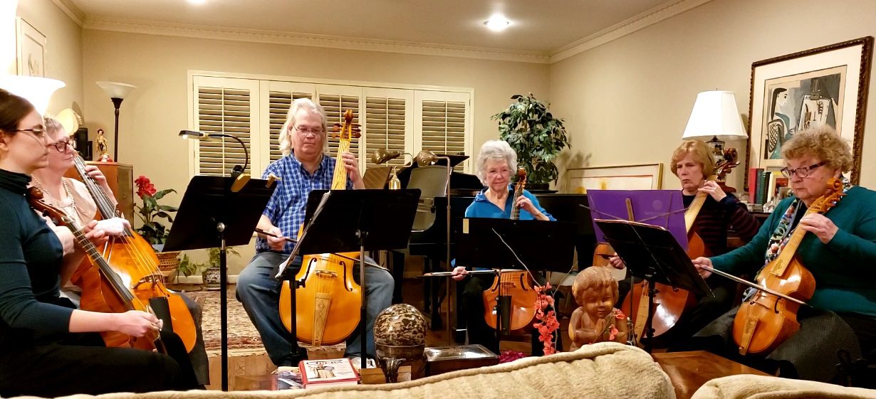 Six people playing cellos in a living room.