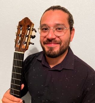 A man with glasses is holding an acoustic guitar.