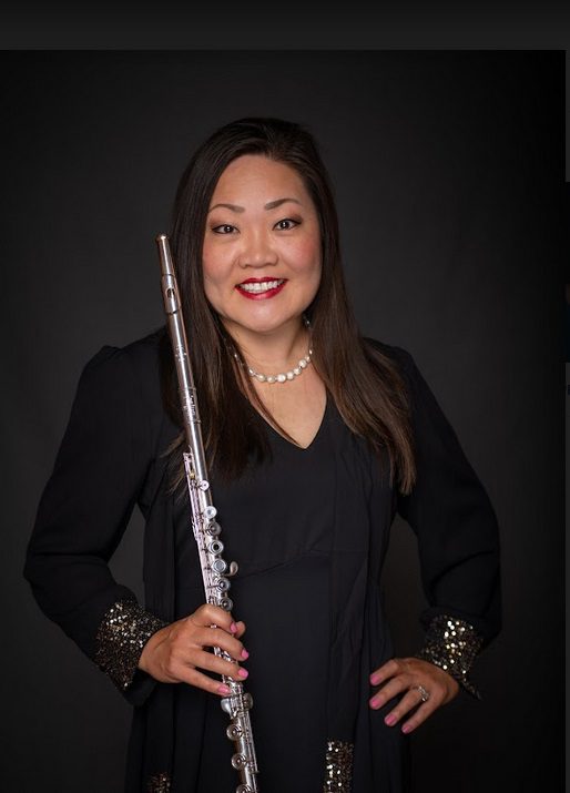 A woman holding a flute in front of a black background.