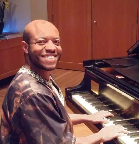 A black man smiling while playing a piano.