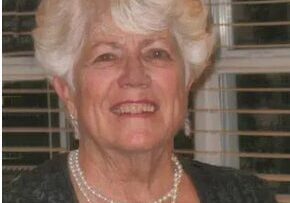 An older woman wearing a black top and pearls.