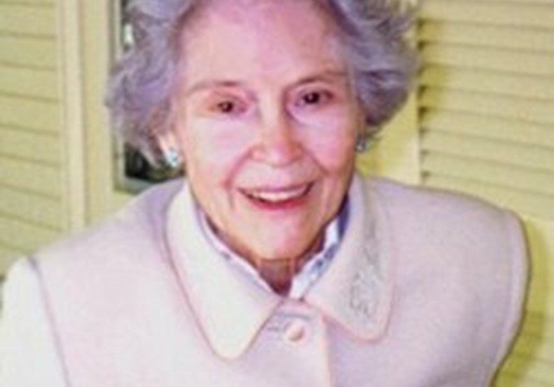 An older woman in a white coat is smiling.