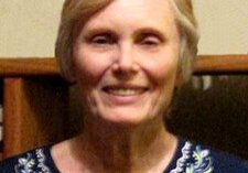 An older woman smiling in front of a bookcase.