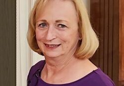 A woman in a purple shirt standing in front of a door.